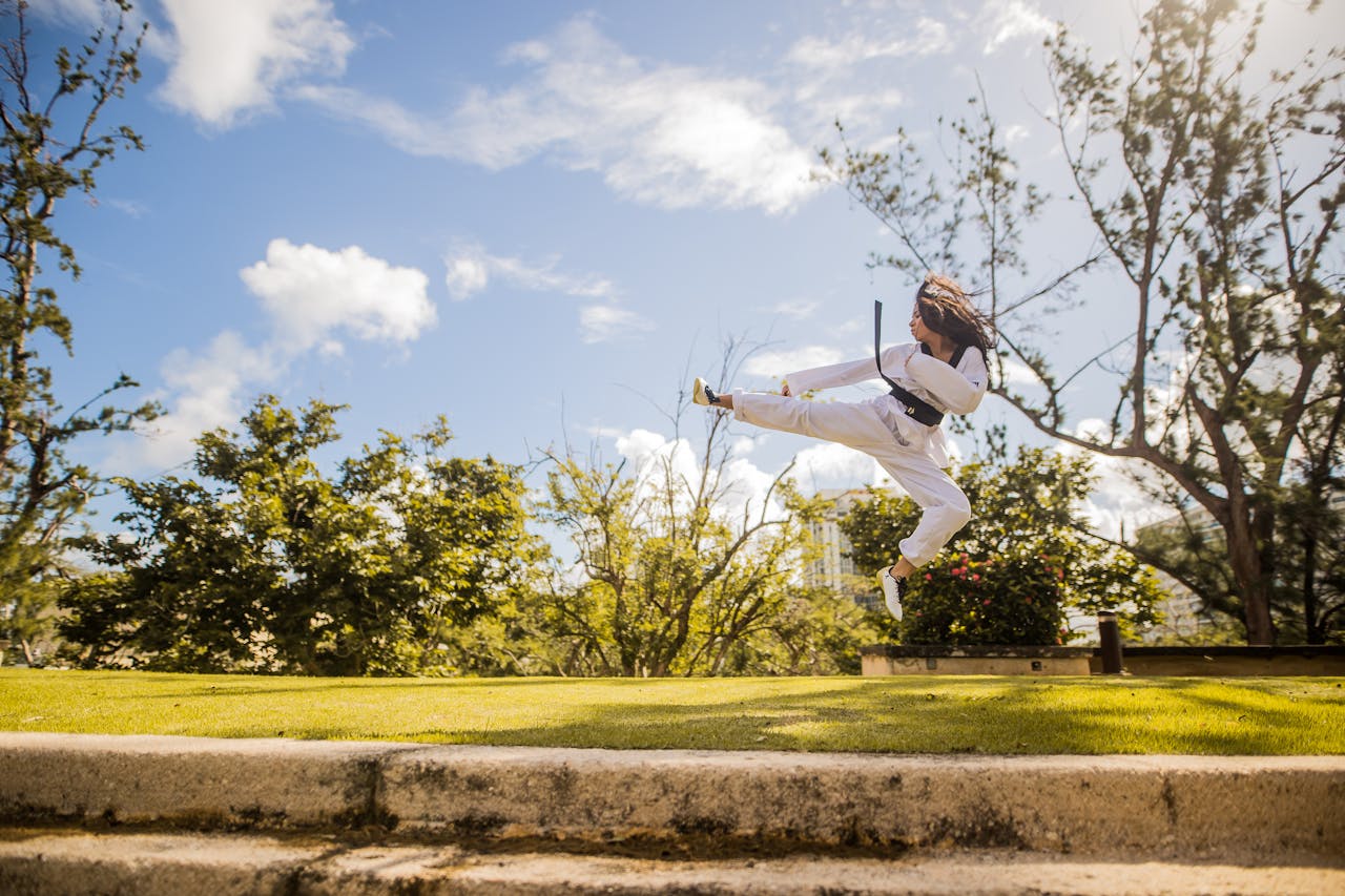 get-in-touch Young woman performs a martial arts kick in a sunny park, showcasing athleticism and focus.
