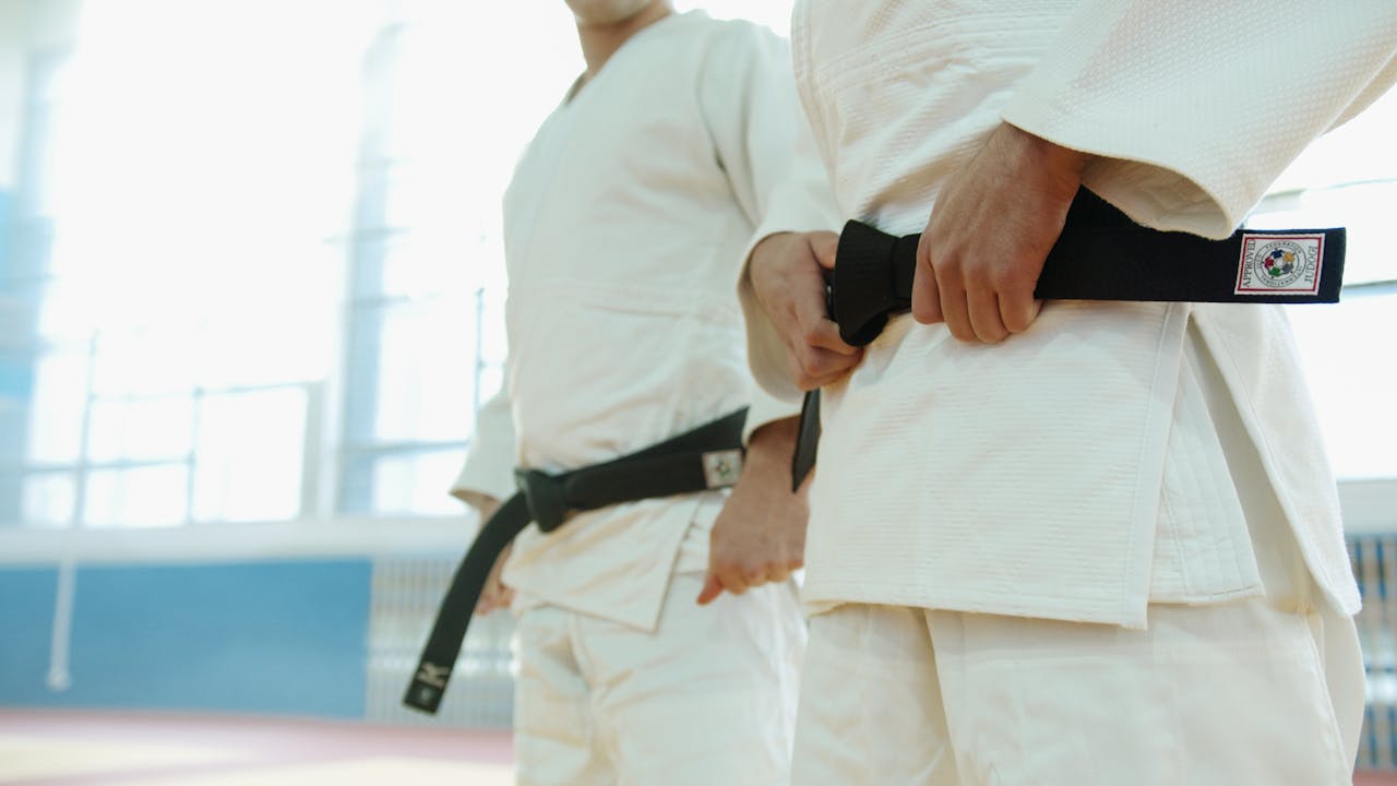 our-story Two martial artists in white uniforms holding black belts, showcasing discipline and strength.